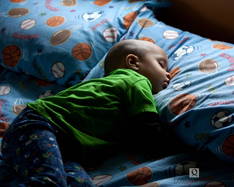 image of young African american boy asleep in bed in pajamas with sunlight.